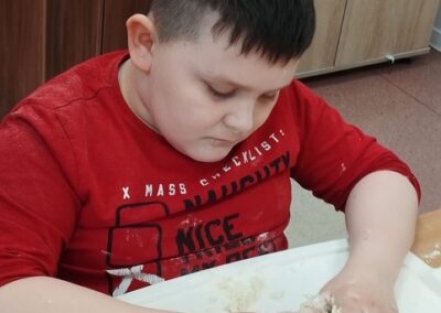 Chłopiec lepi ciasto na stoliku, ubrany w czerwoną koszulkę.