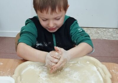 Chłopiec ugniata ciasto na mącznej tacy przy stole.