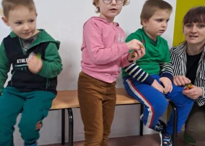 Dzieci i dorosły na ławce z rysunkami klowna na ścianie, tabliczka 19A w tle.