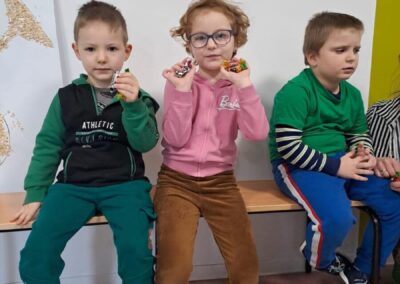Trójka dzieci na ławce; dwoje z słodyczami, jedno w okularach; w tle rysunki klaunów.