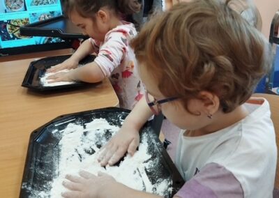 Dzieci na zajęciach kulinarnych w przedszkolu, rozwijają mąkę na tacy.