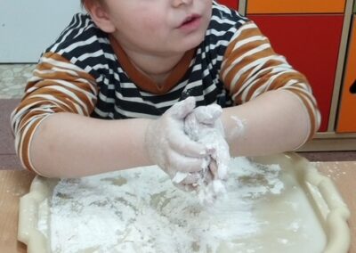 Dziecko w pasiastym swetrze bawi się mąką na plastikowej tacy.