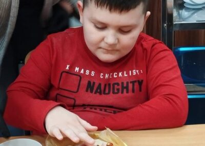 Dziecko w czerwonej koszulce przygotowuje przekąskę przy stole, obok misa ze składnikami.