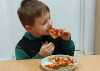 Dziecko przy stole jedzące pizzę, przed nim talerz z kawałkami pizzy i szklanka.