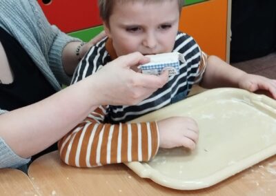 Dziecko siedzi przy stole, dorosły trzyma masło, w tle kolorowa szafka.