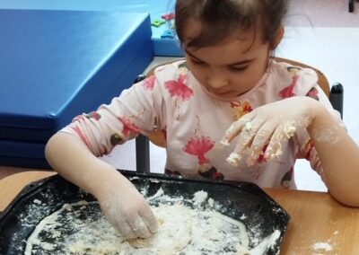 Dziewczynka bawi się mąką na czarnej tacy przy stole w pokoju.