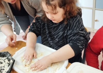 Dziewczynka ugniata ciasto na tacy, kobieta pomaga obok.