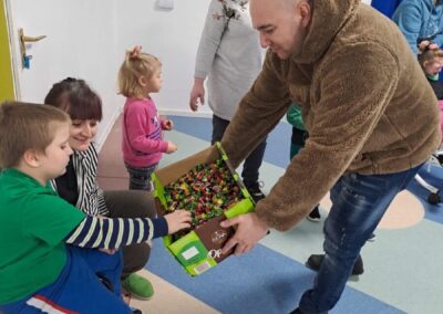 Mężczyzna w futrzanej kurtce rozdaje dzieciom słodycze w przedszkolu, kolorowe dekoracje na ścianach.