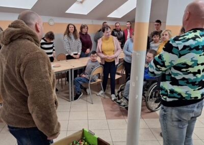 Grupa ludzi w jasnym pomieszczeniu wokół stołu, na pierwszym planie znajdują się pudełka cukierków.