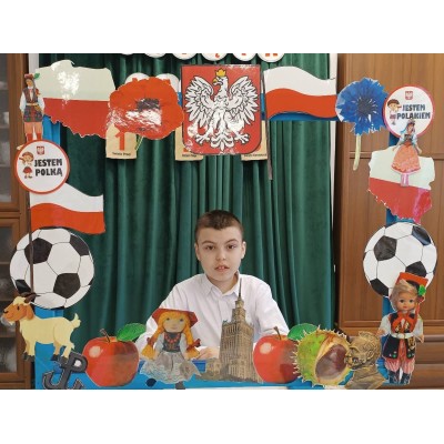 Chłopiec za dekoracyjną ramą z polskimi symbolami, flagą, godłem i napisami Jestem Polką i Jestem Polakiem.
