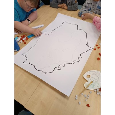 Dzieci przy stole wykonujące mapę z białych i czerwonych kawałków papieru na dużym arkuszu.