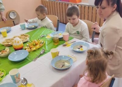 Dzieci jedzą zupę przy udekorowanym stole, w tle kolorowe klocki do zabawy.