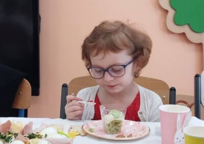 Dziecko w okularach przy stole z jedzeniem, kwiatowe dekoracje w tle.