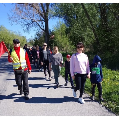Grupa osób idzie wzdłuż drogi otoczonej zielenią, prowadzona przez mężczyznę z czerwoną flagą.