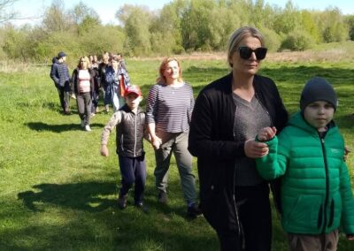 Grupa osób idzie ścieżką przez zieloną łąkę w słoneczny dzień.