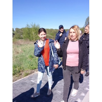 Grupa osób spaceruje po chodniku obok zielonego terenu w słoneczny dzień.
