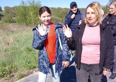 Grupa osób spaceruje po chodniku obok zielonego terenu w słoneczny dzień.