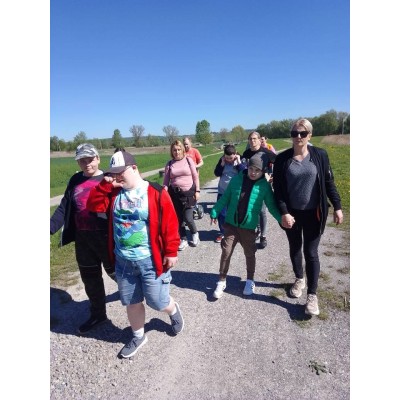 Grupa osób spaceruje ścieżką na łonie natury w słoneczny dzień.