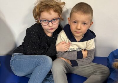 Dwoje dzieci siedzi obok siebie na niebieskiej powierzchni, patrząc w stronę aparatu.