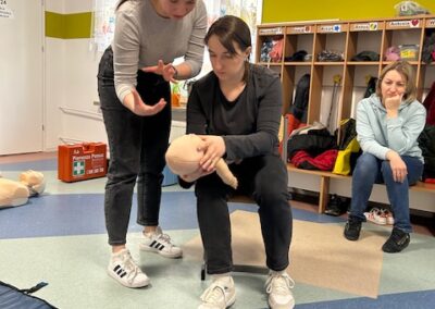 Group learning infant CPR with manikin, women demonstrating and observing attentively.