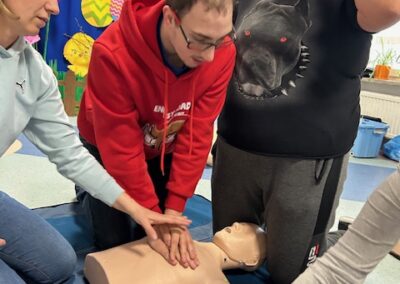 Trening z pierwszej pomocy z użyciem manekina i defibrylatora AED w grupie ćwiczących osób.