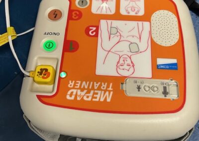 Przenośny trenażer AED do nauki resuscytacji z oznaczeniami przycisków i instrukcjami elektrod.