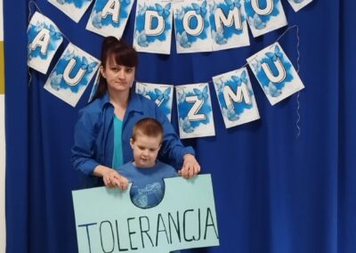 Kobieta i dziecko przed niebieską kurtyną z hasłem "Dzień Świadomości Autyzmu".