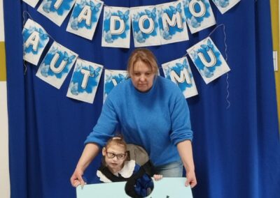 Kobieta i dziecko z puzzle "MIŁOŚĆ" na tle banera Dnia Świadomości Autyzmu.