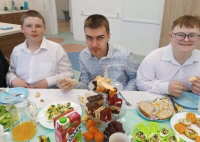 Trzy osoby siedzą przy stole z jedzeniem na przyjęciu; elegancko ubrane.