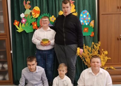Pięciu chłopców przed wielkanocną dekoracją z napisem "Wielkanoc" i kolorowymi elementami.