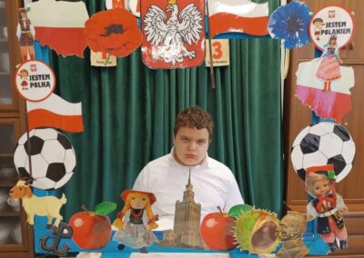 Chłopiec siedzi za stołem z dekoracjami symbolizującymi Polskę i polską kulturę.