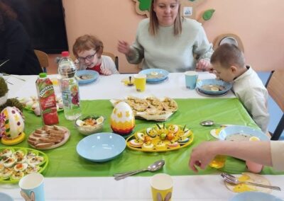 Grupa przy stole z ozdobami i świątecznym jedzeniem, w tym jajka faszerowane, pieczywo.