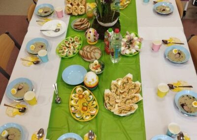 Stół na świąteczne przyjęcie z zielonym bieżnikiem, potrawami, pisankami i napojami.