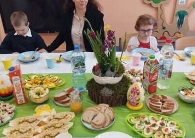 Na stole świąteczne śniadanie z jajkami i pieczywem, dekoracje, przy stole dzieci i dorosły.