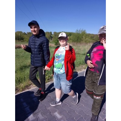 Trzech chłopców idących po chodniku w letnich ubraniach na tle zieleni i niebieskiego nieba.