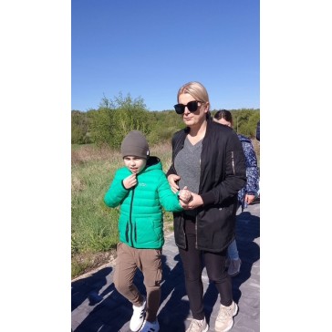 Kobieta w czarnej kurtce z okularami trzyma chłopca w zielonej kurtce za rękę podczas spaceru.