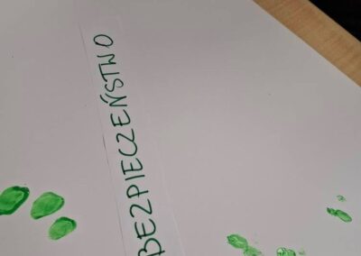 Kartka z napisem bezpieczenstwo i zielone odciski palców oraz dłoni na białej powierzchni.