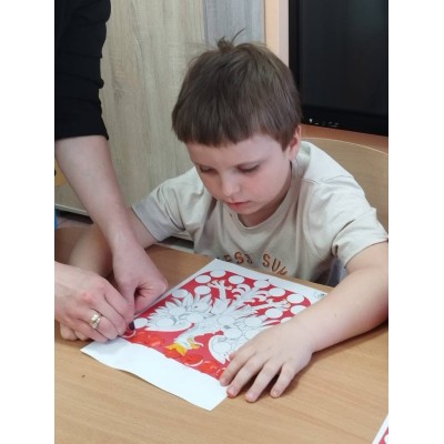 Chłopiec koloruje obrazek drzewa z owocami, dorosła osoba pomaga mu trzymać kartkę.