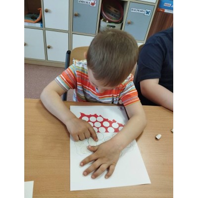 Chłopiec nakleja białe kółka na konturze mapy Polski na kartce papieru przy stole.