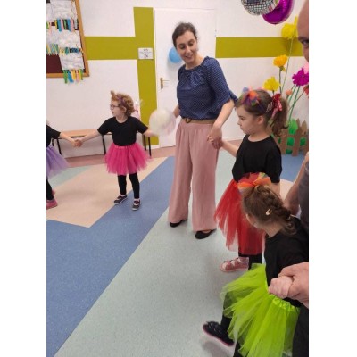 Dzieci i dorosły trzymający się za ręce w kolorowo udekorowanym pomieszczeniu podczas zajęć.