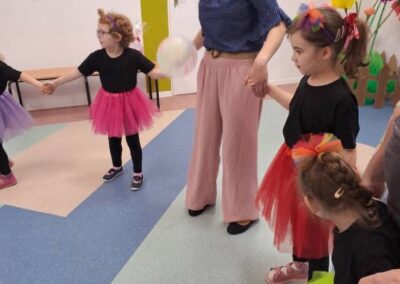 Dzieci i dorosły trzymający się za ręce w kolorowo udekorowanym pomieszczeniu podczas zajęć.