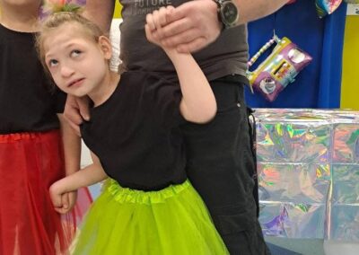 Dwoje dzieci w kolorowych tiulowych spódnicach z dorosłym mężczyzną na przyjęciu z balonami.