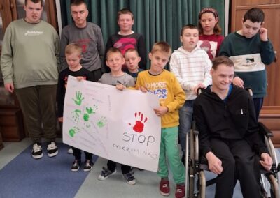 Grupa dzieci z plakatem z napisem STOP DYSKRYMINACJI, w tym chłopiec na wózku.