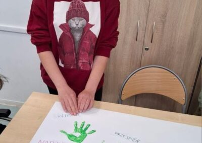 Dziewczynka tworzy plakat z zielonymi odciskami dłoni i słowami nadzieja, przyjaźń, wsparcie, bezpieczeństwo, tolerancja.