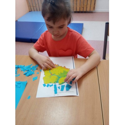Dziewczynka nakleja niebieskie kawałki papieru na mapę siedząc przy stole.