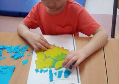 Dziewczynka nakleja niebieskie kawałki papieru na mapę siedząc przy stole.
