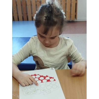 Dziewczynka wskazuje palcem na ilustrację konturu Polski z częściowo wypełnionymi kołami.