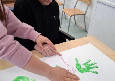 Chłopiec i dorosła osoba robią zielone odbitki dłoni na papierze z napisami markerem.
