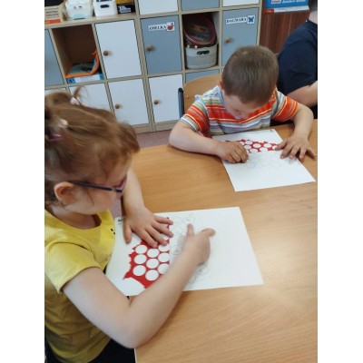 Dwoje dzieci wypełnia karty pracy ze wzorem okręgów przy stole w sali z szafkami.