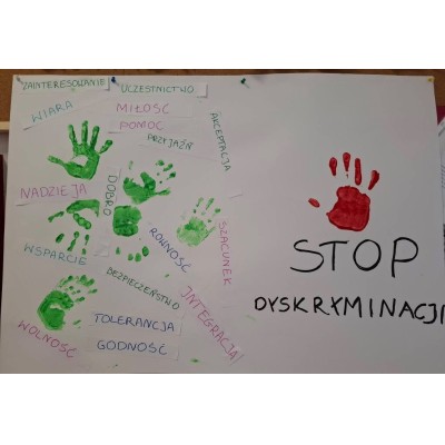 Plakat z zielonymi odciskami dłoni i słowami wartości oraz czerwonym odciskiem i napisem STOP DYSKRYMINACJI.